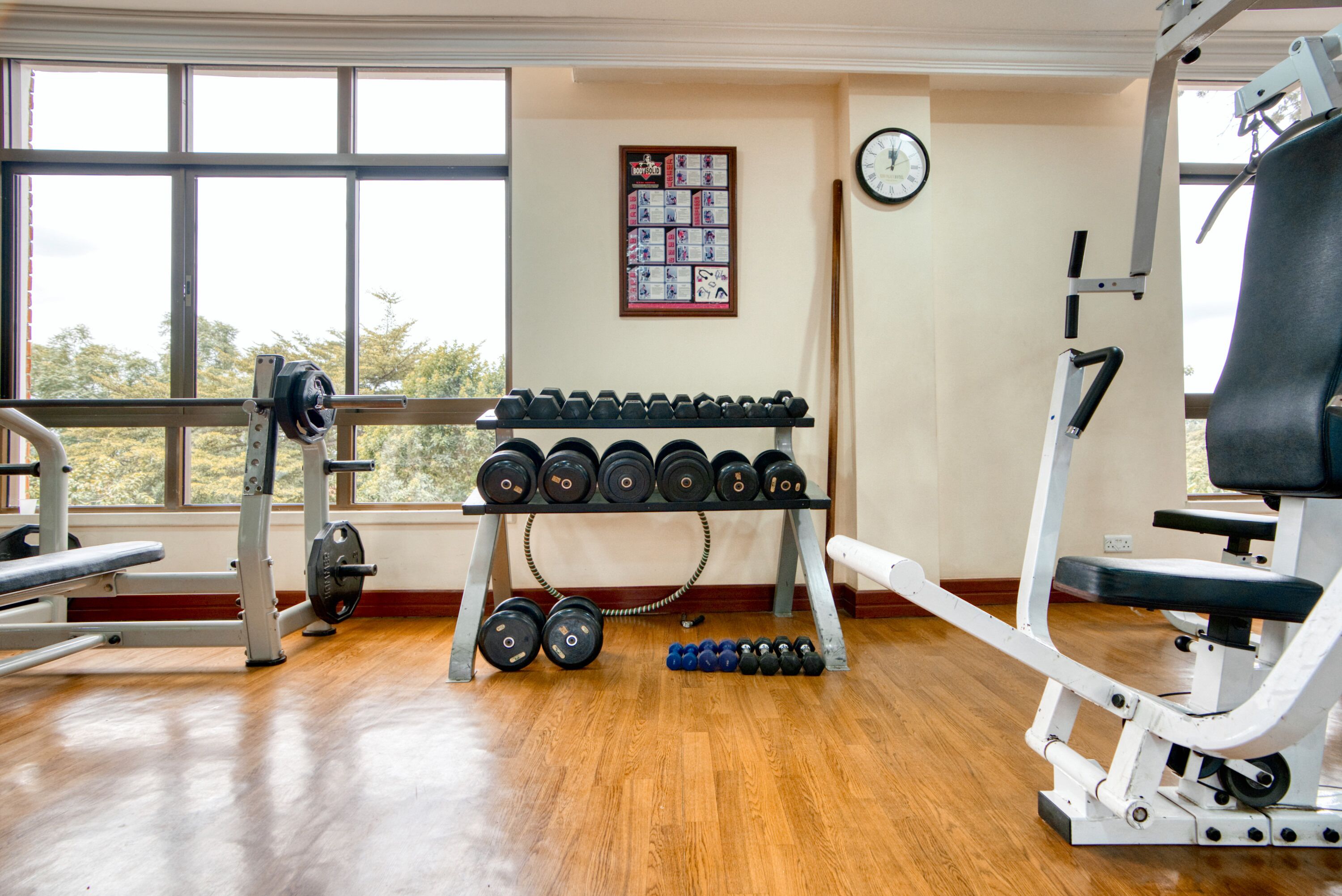 A gym with weightlifting equipment, a rack of dumbbells, and a wall clock.