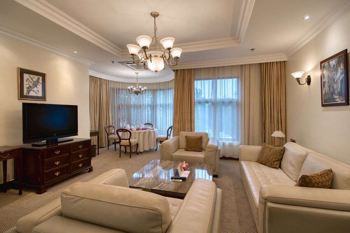 A spacious living room with a flat-screen TV, leather sofas, a coffee table, and a chandelier.