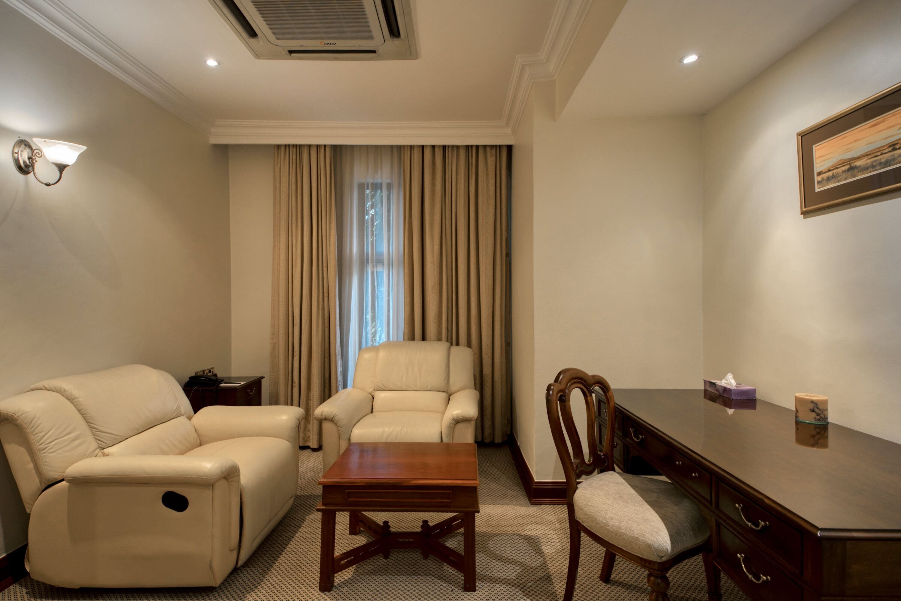 A room with a leather sofa, a wooden coffee table, a wooden desk, and a chair.