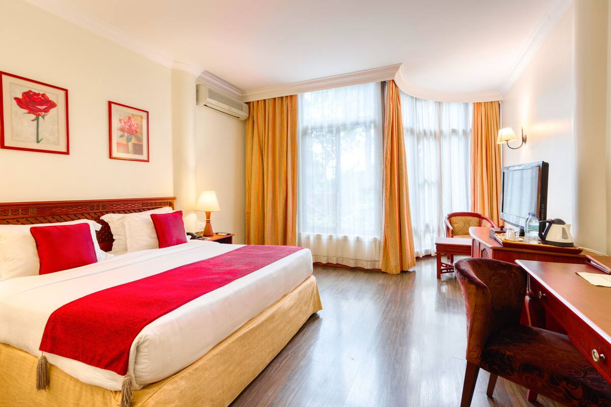 A hotel room with a large bed, a desk, a chair, a television, and two framed pictures on the wall.