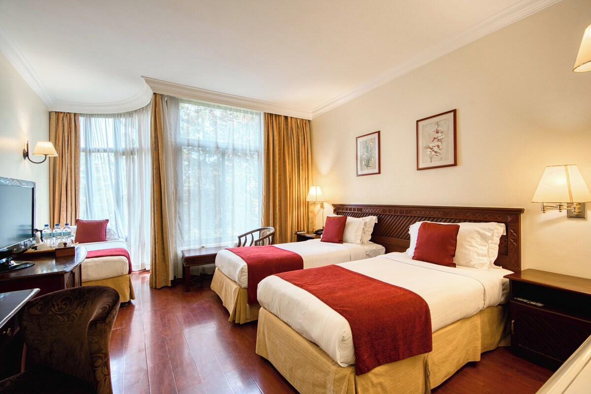 A hotel room with two beds, a desk, a chair, a TV, and a window with curtains.