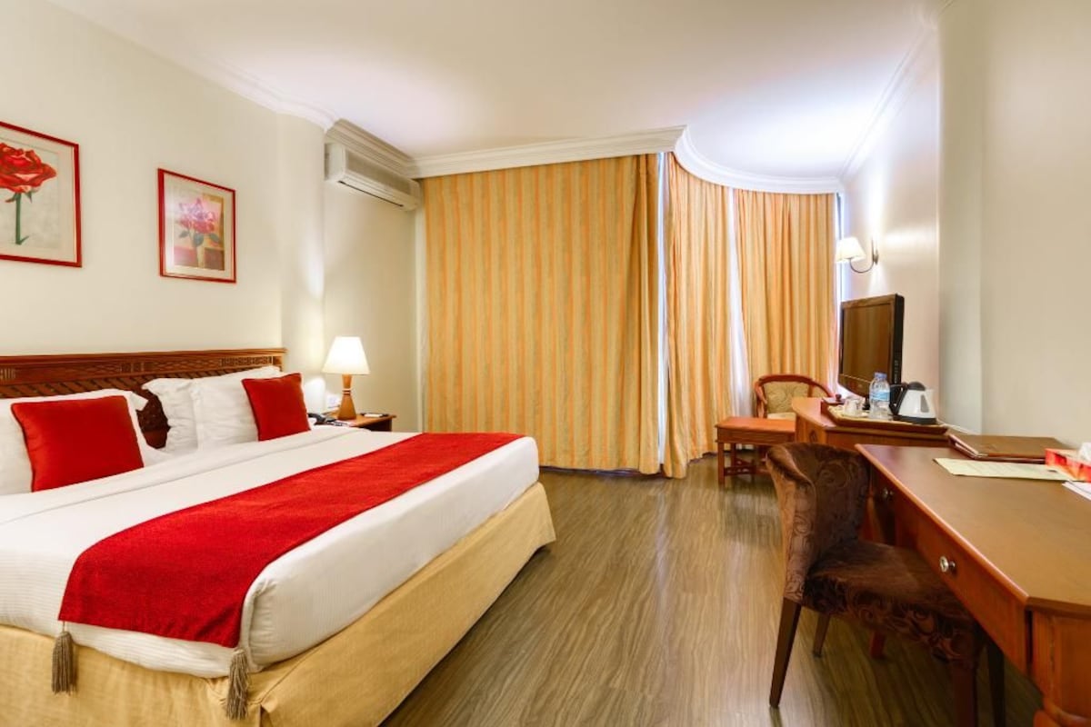 Habitación de hotel con cama, escritorio, silla, televisión y ventana con cortinas.
