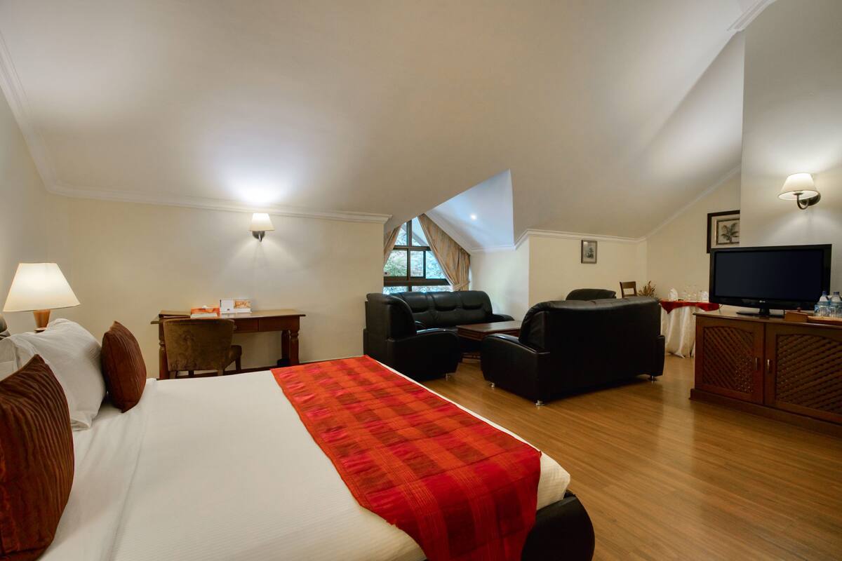 A hotel room with a large bed, a desk, a television, and a seating area.