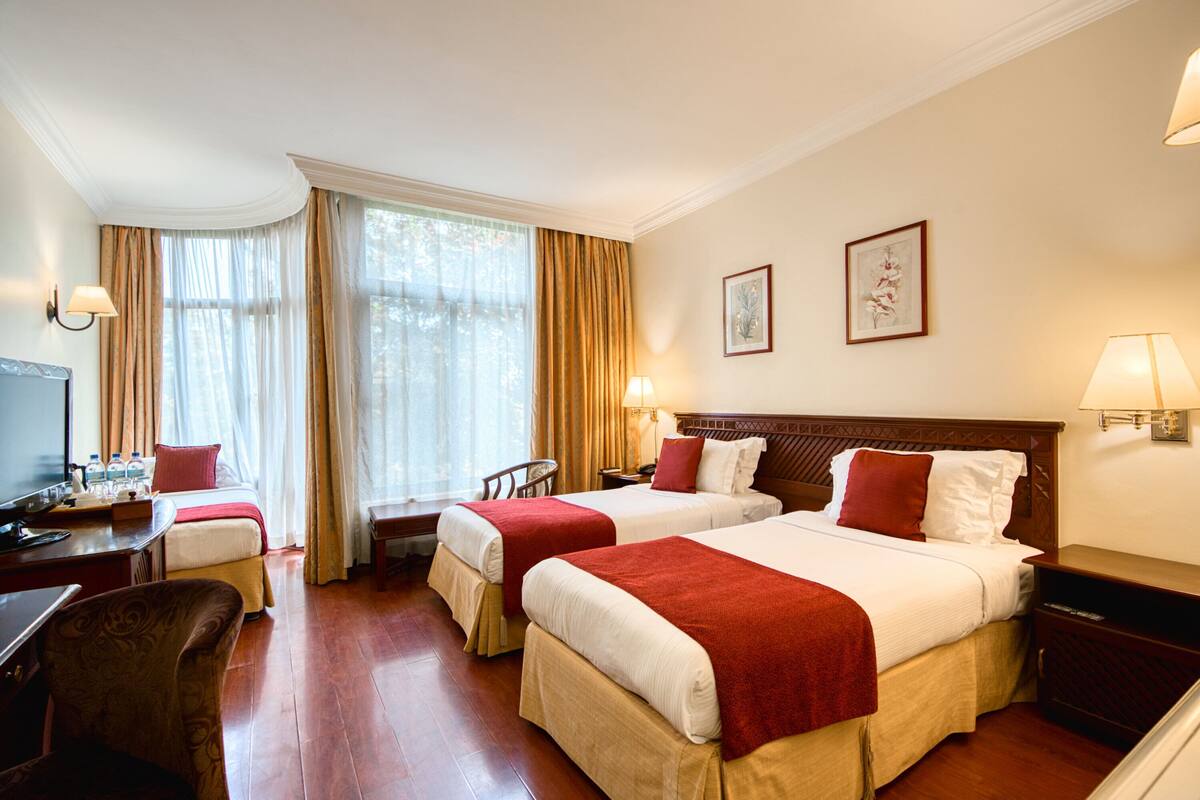 A hotel room with two beds, a desk, a chair, a TV, and a window with curtains.