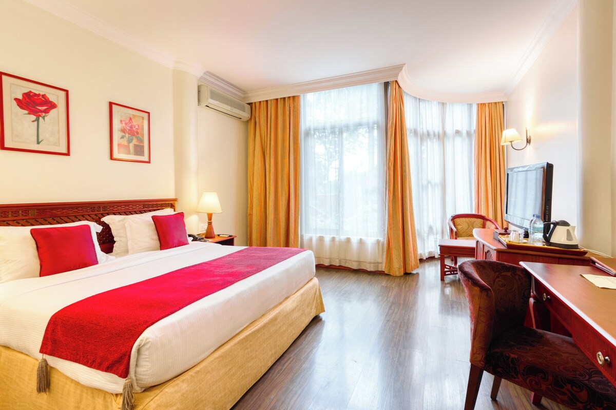 A hotel room with a large bed, a desk, a chair, a television, and two framed pictures on the wall.