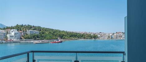 Varanda com mesa e cadeira, vista para um corpo de água com um barco vermelho e um horizonte urbano ao fundo.