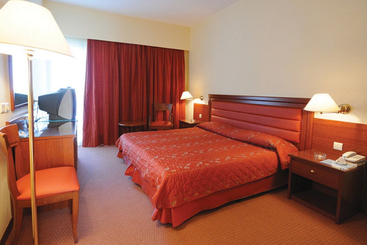 A hotel room with a bed, desk, chair, and two bedside lamps.