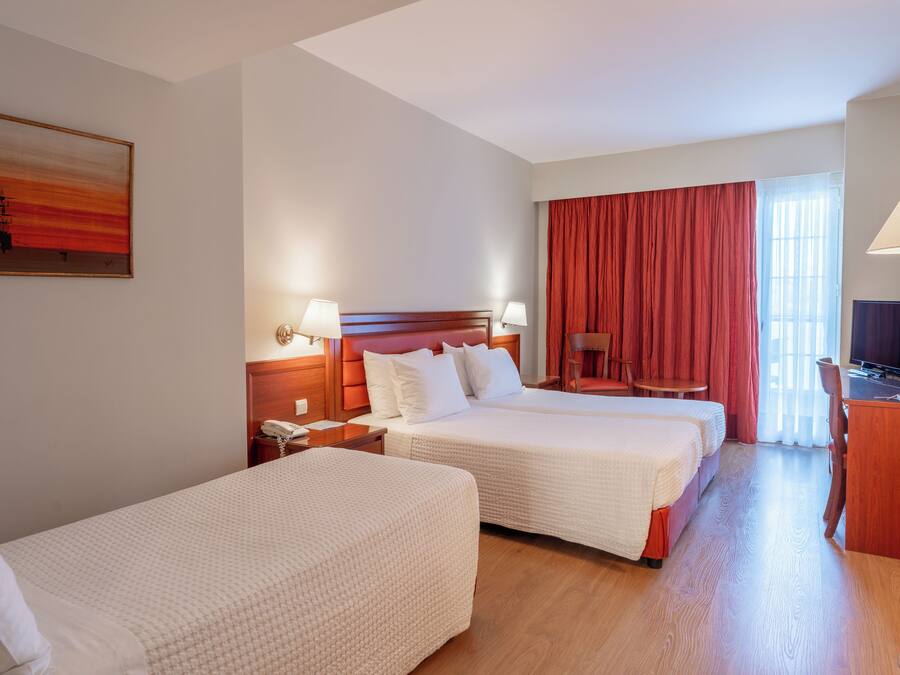 Habitación de hotel con dos camas, un escritorio con televisor, una silla y un cuadro en la pared.