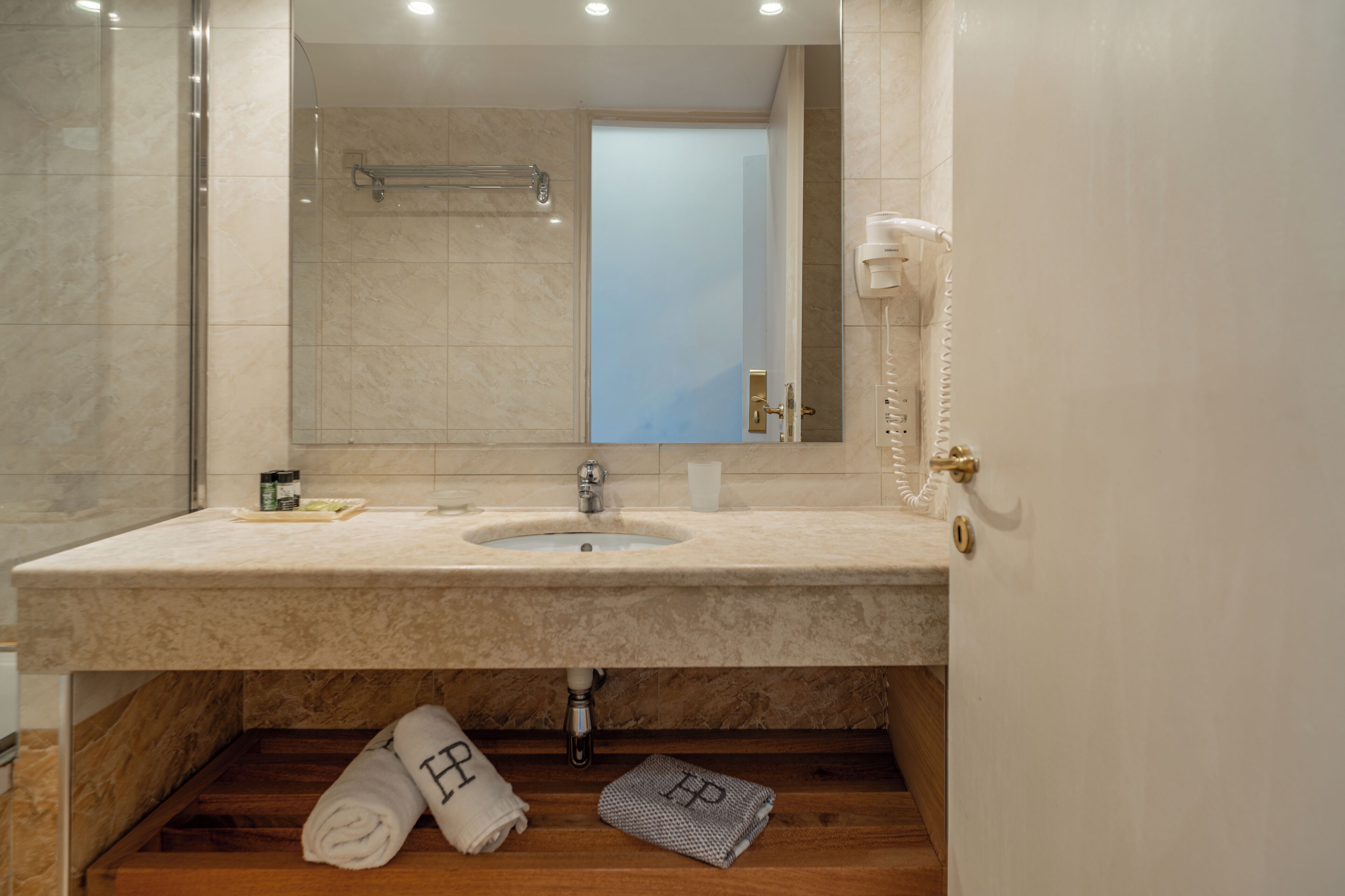 Un baño con lavamanos de mármol, cabina de ducha de vidrio y un perchero para toallas.
