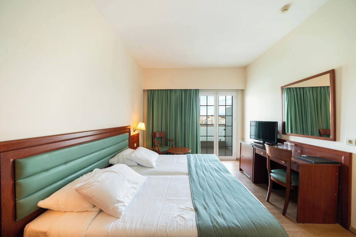 Ein Hotelzimmer mit zwei Betten, einem Schreibtisch, einem Sessel, einem Fernseher und einer Schiebetür zum Außenbereich.
