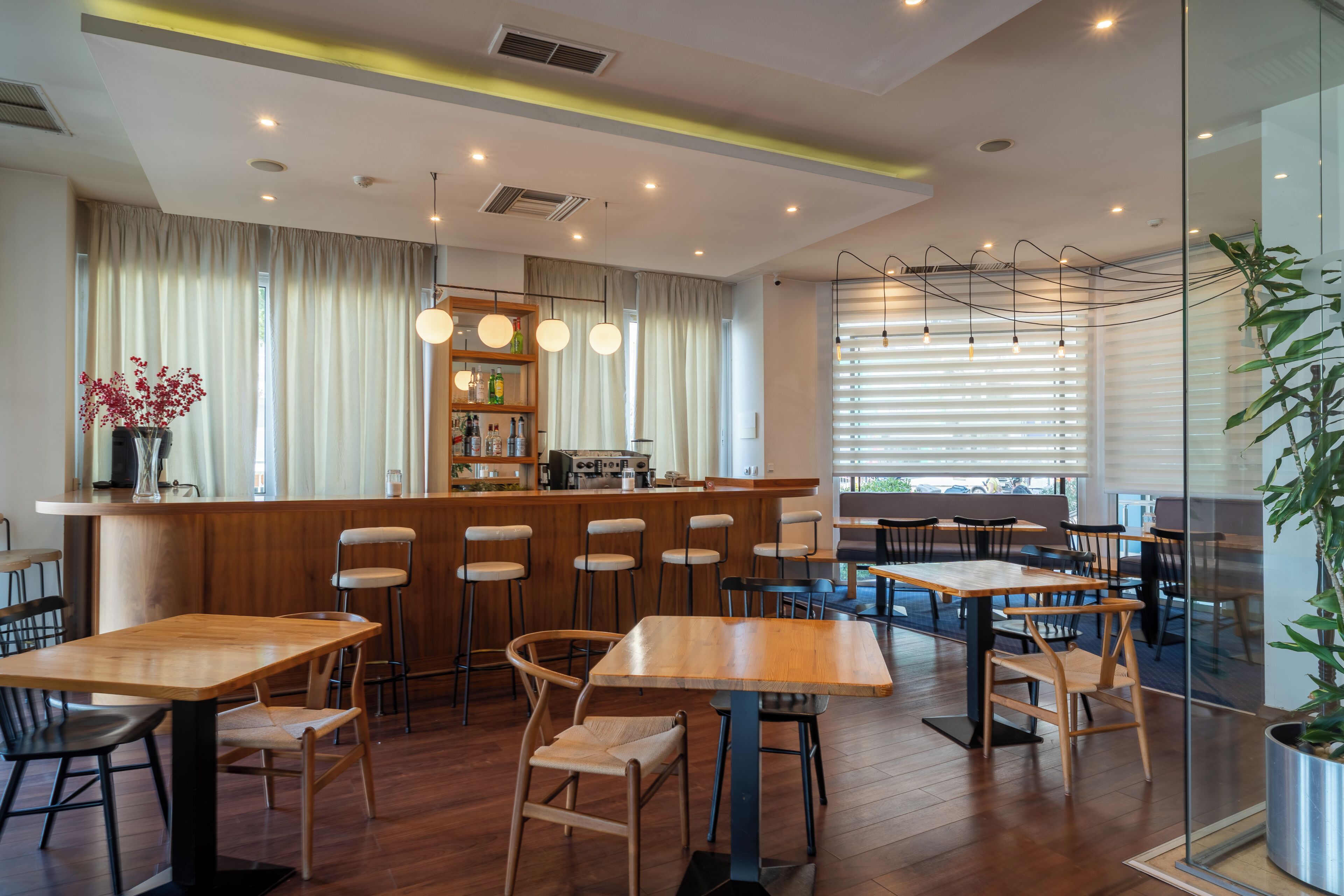 Interior de restaurante con mesas y sillas de madera, una zona de bar y vistas a la calle.