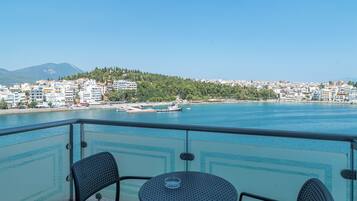 A balcony with two chairs and a table overlooking a body of water with boats, a cityscape, and a mountain in the distance.