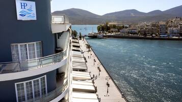 A waterfront hotel with balconies, a poolside area, and a view of boats and mountains.