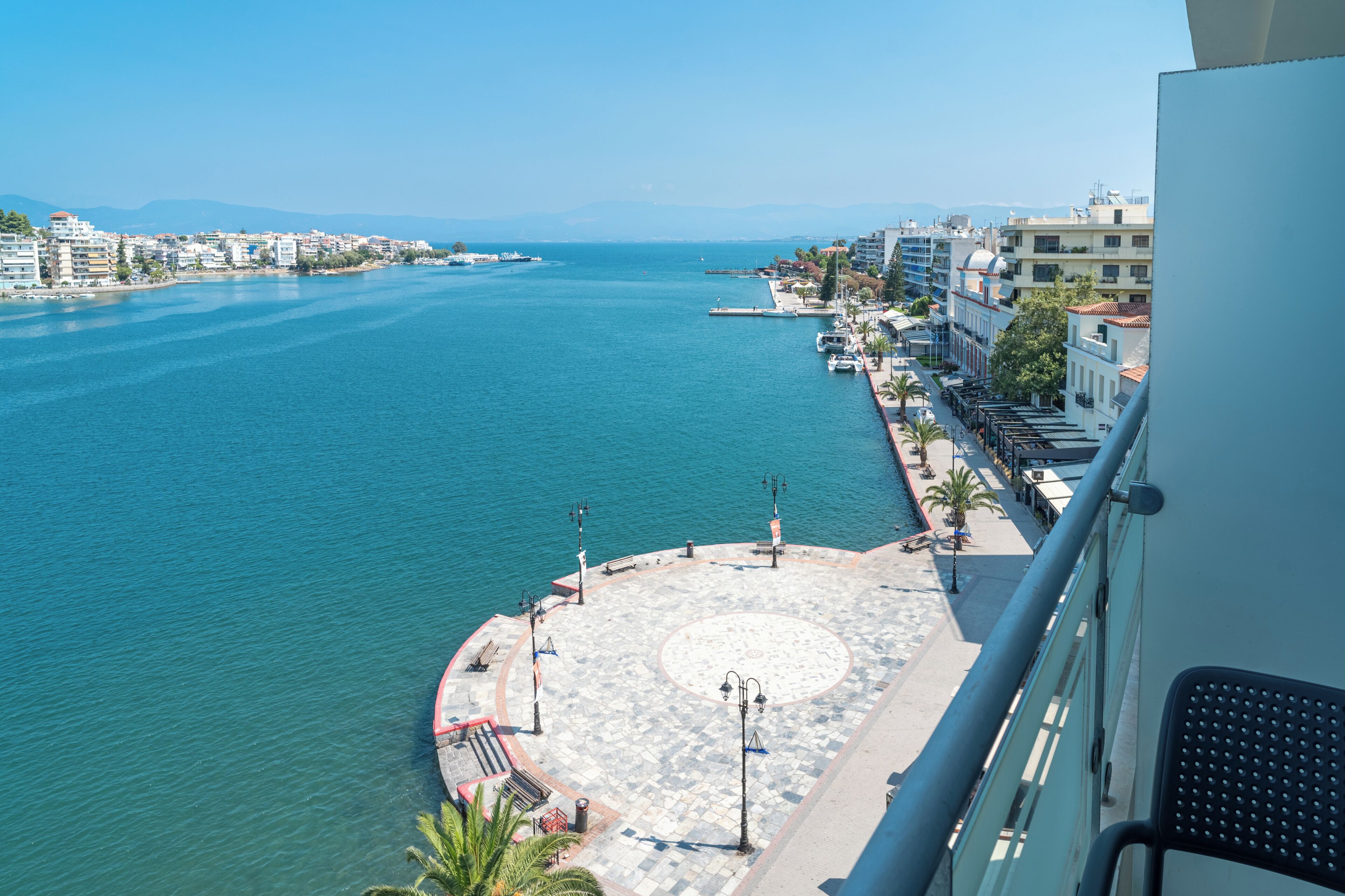 Eine Küstenstadt mit einem Yachthafen, Gebäuden entlang der Uferlinie und einer Promenade mit Bänken und Laternen.