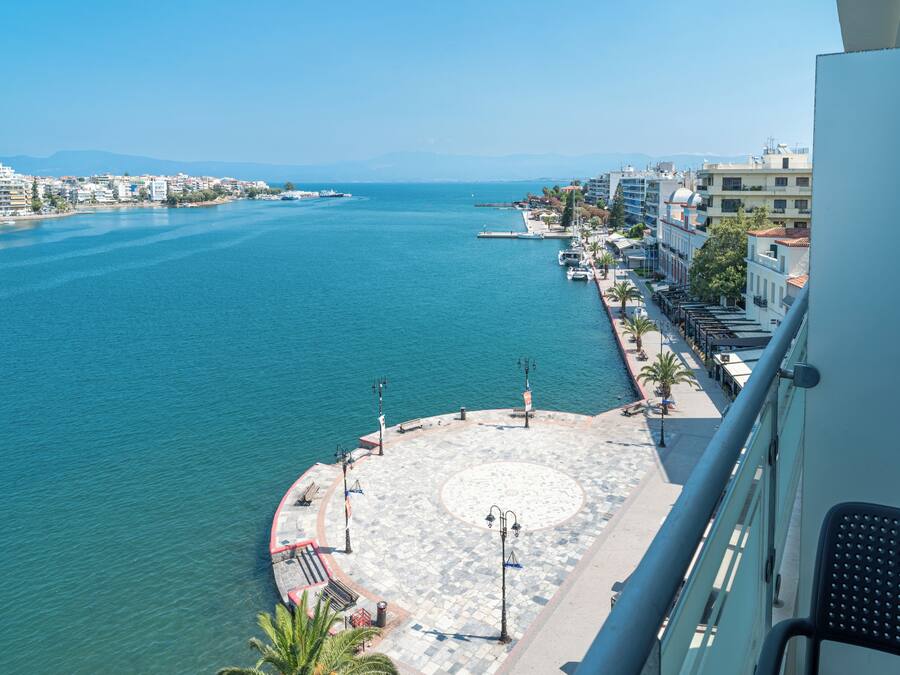 Een kuststadsgezicht met een jachthaven, gebouwen langs de waterkant en een promenade met bankjes en lantaarns.