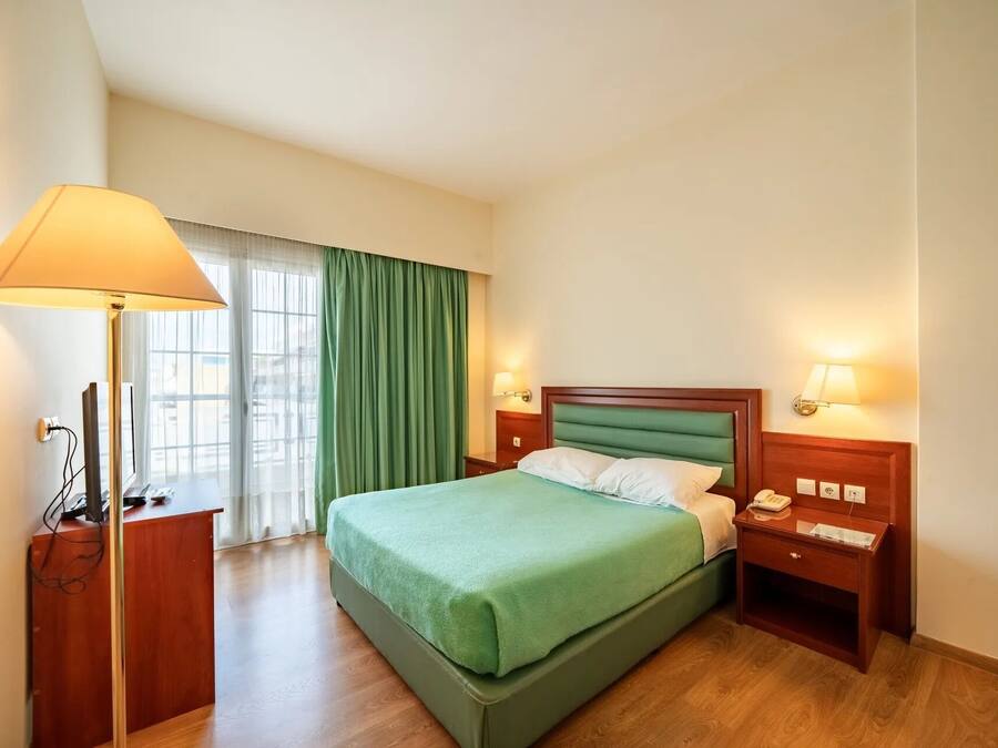 Una habitació d'hotel amb un llit, làmpades de nit, un escriptori amb un telèfon i una finestra amb cortines.