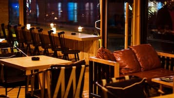 An indoor seating area with wooden tables and chairs, a leather couch, and a view of the street outside.