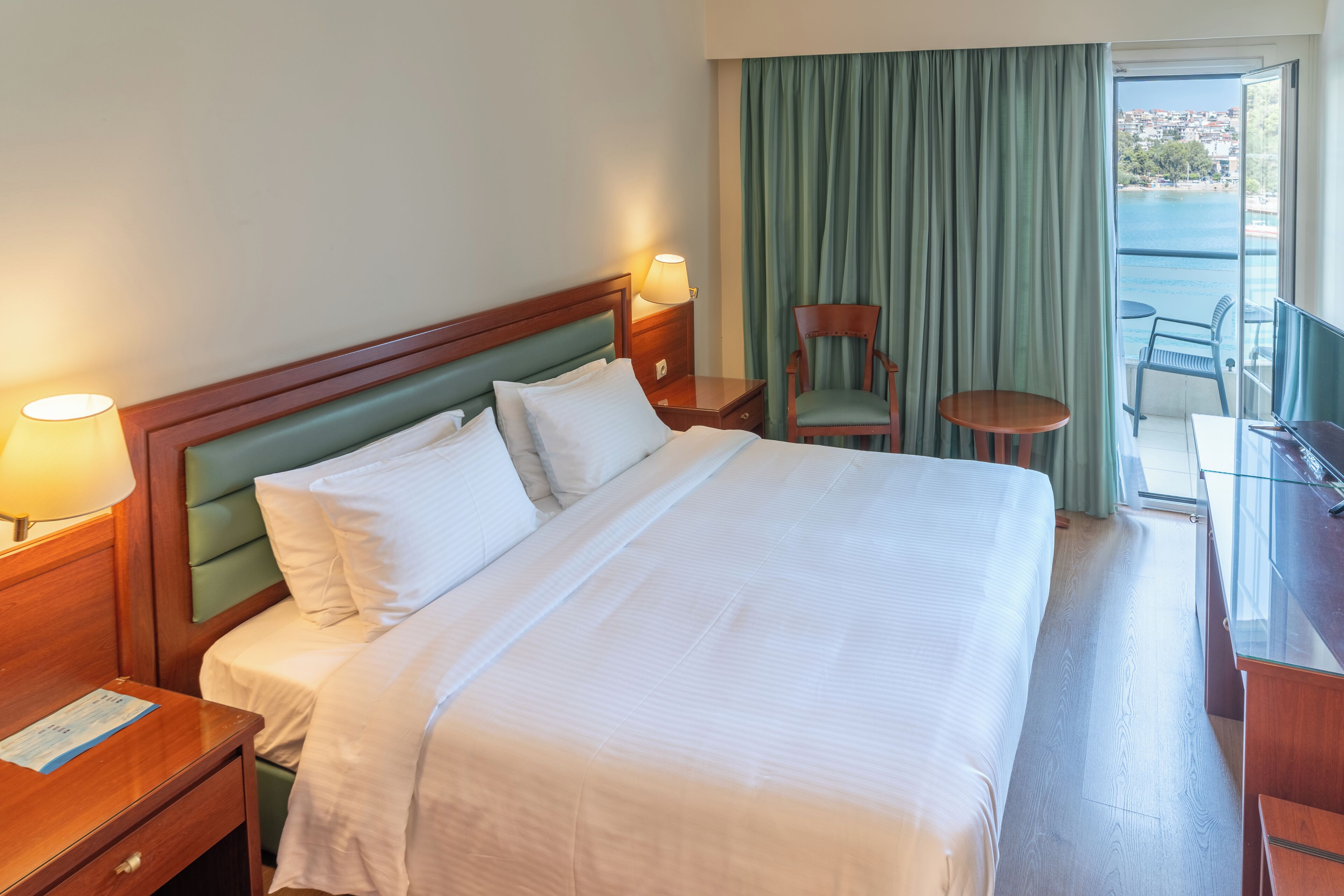 Habitación de hotel con una cama grande, un escritorio con una silla, una mesita y vista al mar a través de una ventana.