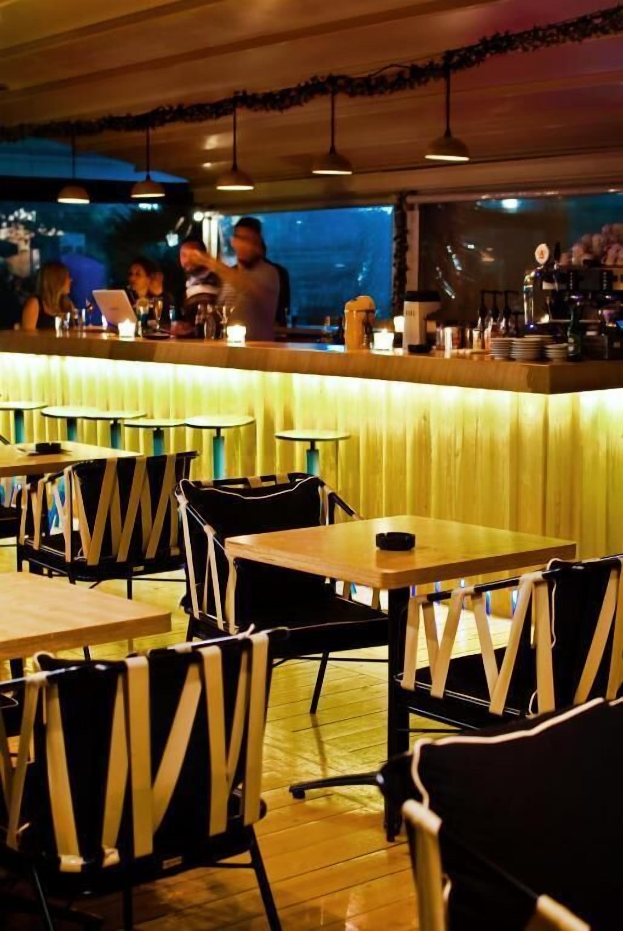 Un espace bar avec des tables et des chaises, un comptoir où se tiennent les employés, et une vue sur l’extérieur.
