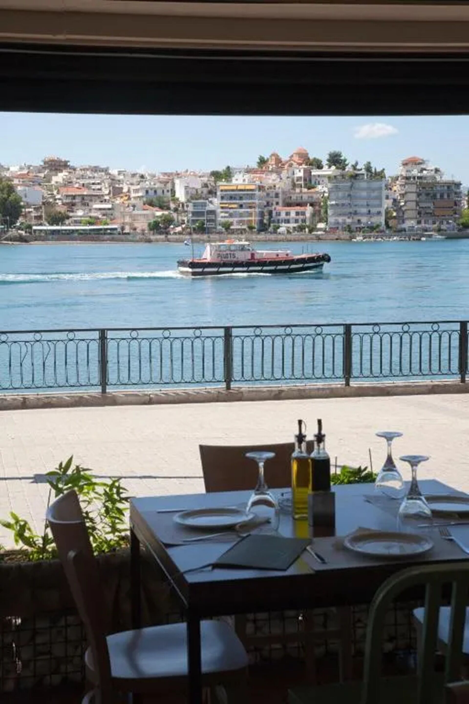 A waterfront restaurant with a table set for dining, overlooking a river with a boat passing by.