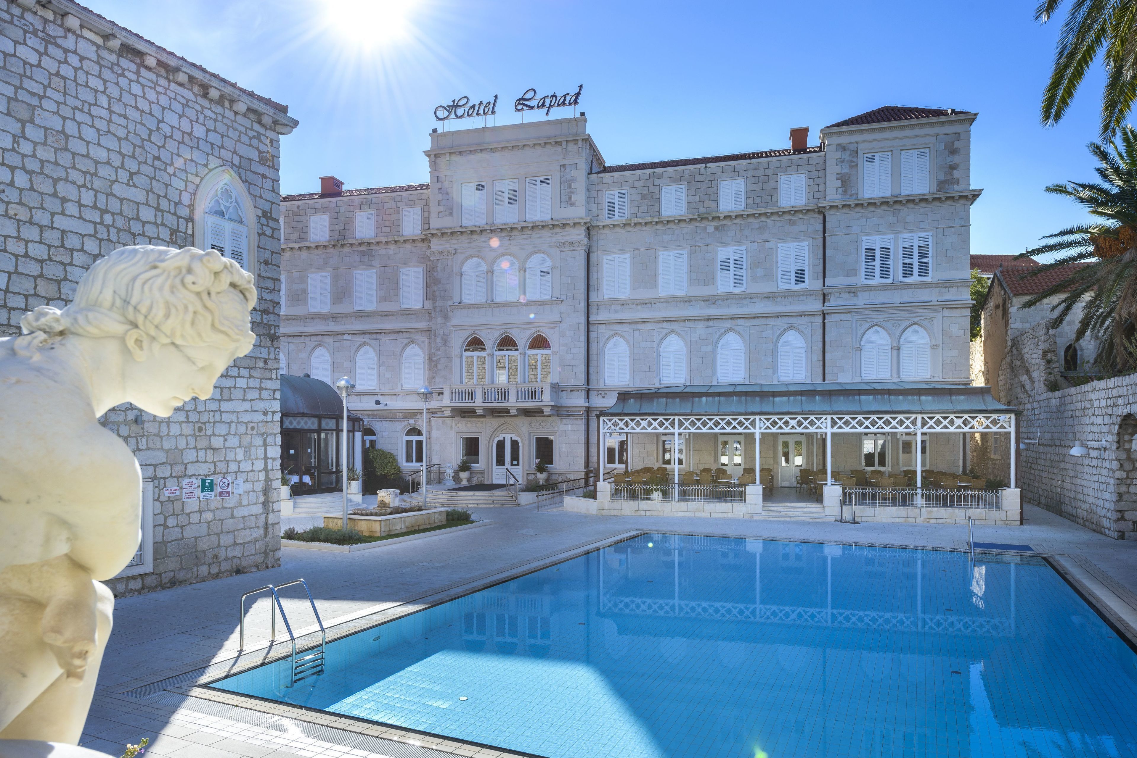 Un hôtel doté d’une piscine, d’une façade en pierre et d’une statue de lion.