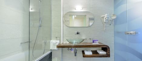 Un baño moderno con ducha envuelta en vidrio, tocador de madera con lavabo de cristal y espejo sobre el lavabo.