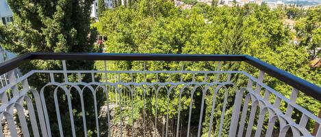A balcony with two black chairs and a white railing, overlooking a green landscape and buildings.