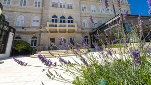 A historic building with a grand entrance, steps leading up to the main doors, and a lush garden with lavender. - Hotel Lapad (Dubrovnik)