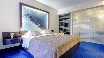 Una habitación de hotel moderna con una cama grande, una mesita de noche, un televisor montado en la pared y un armario.