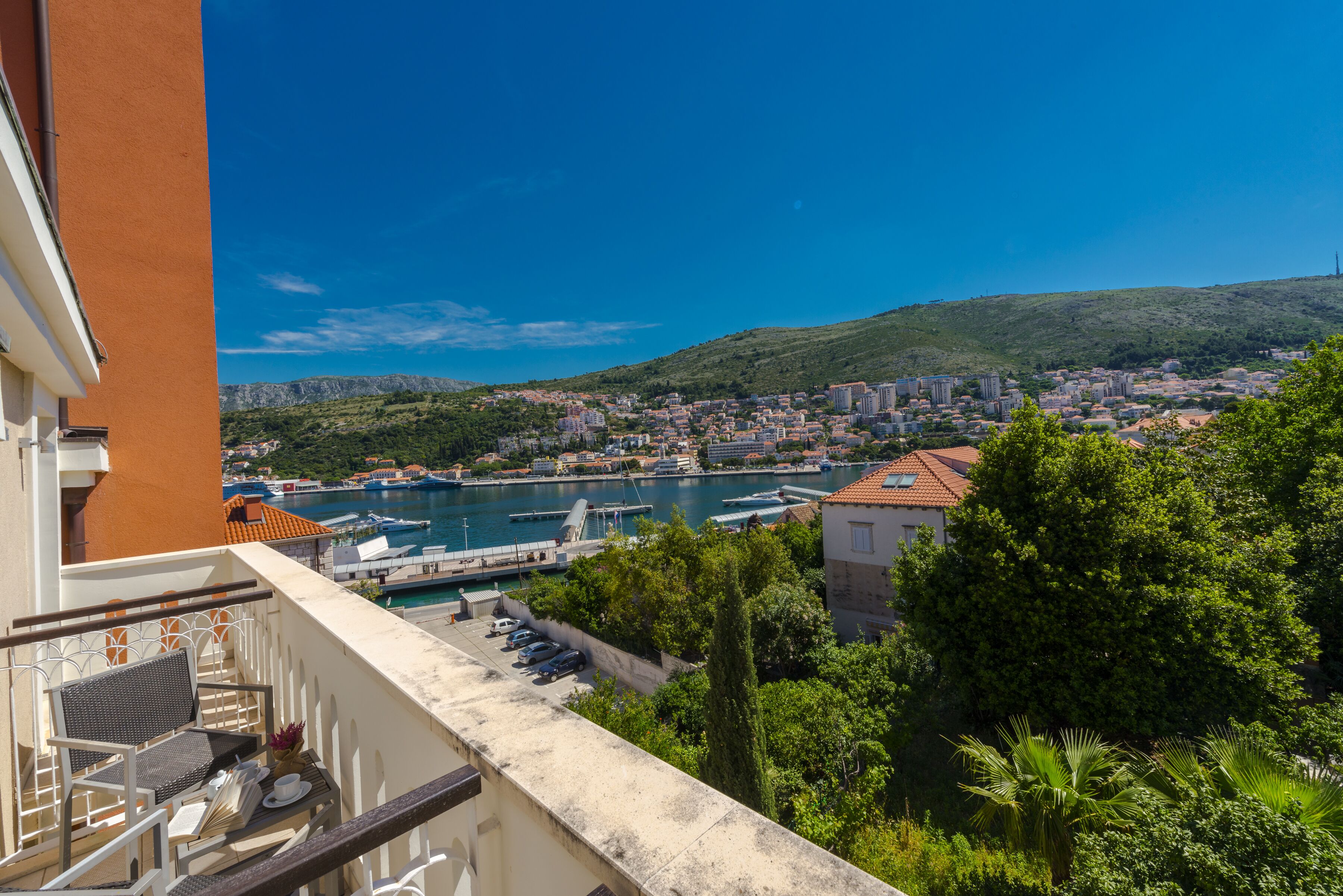 A balcony with a table and chairs overlooking a marina with boats and a town in the background.