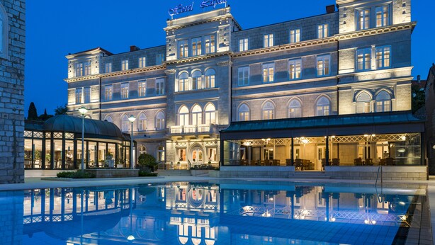 A large hotel with a reflective pool and a well-lit facade. - Hotel Lapad (Dubrovnik)