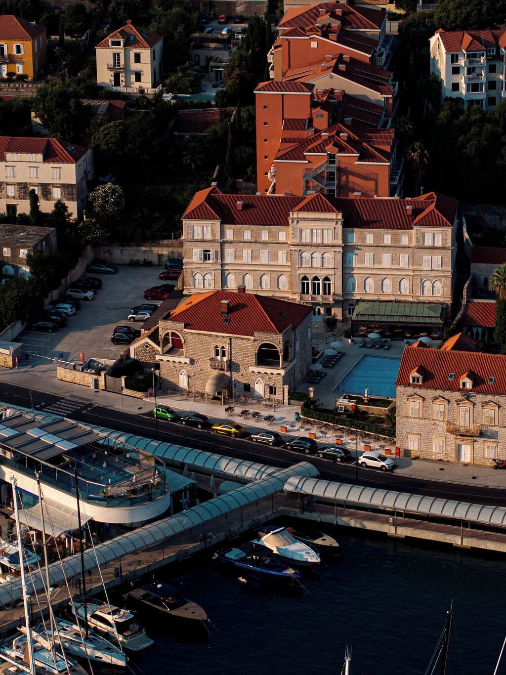 Une ville côtière dotée d’un port de plaisance, de bâtiments en pierre aux toits rouges et d’un grand bâtiment aux fenêtres en arc de cercle.