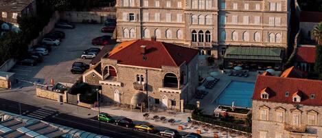 A coastal town with a marina, stone buildings with red roofs, and a large building with arched windows.