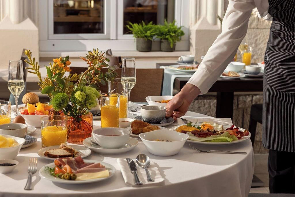 Una mesa de desayuno preparada con diferentes platos, bebidas y un jarrón de flores.