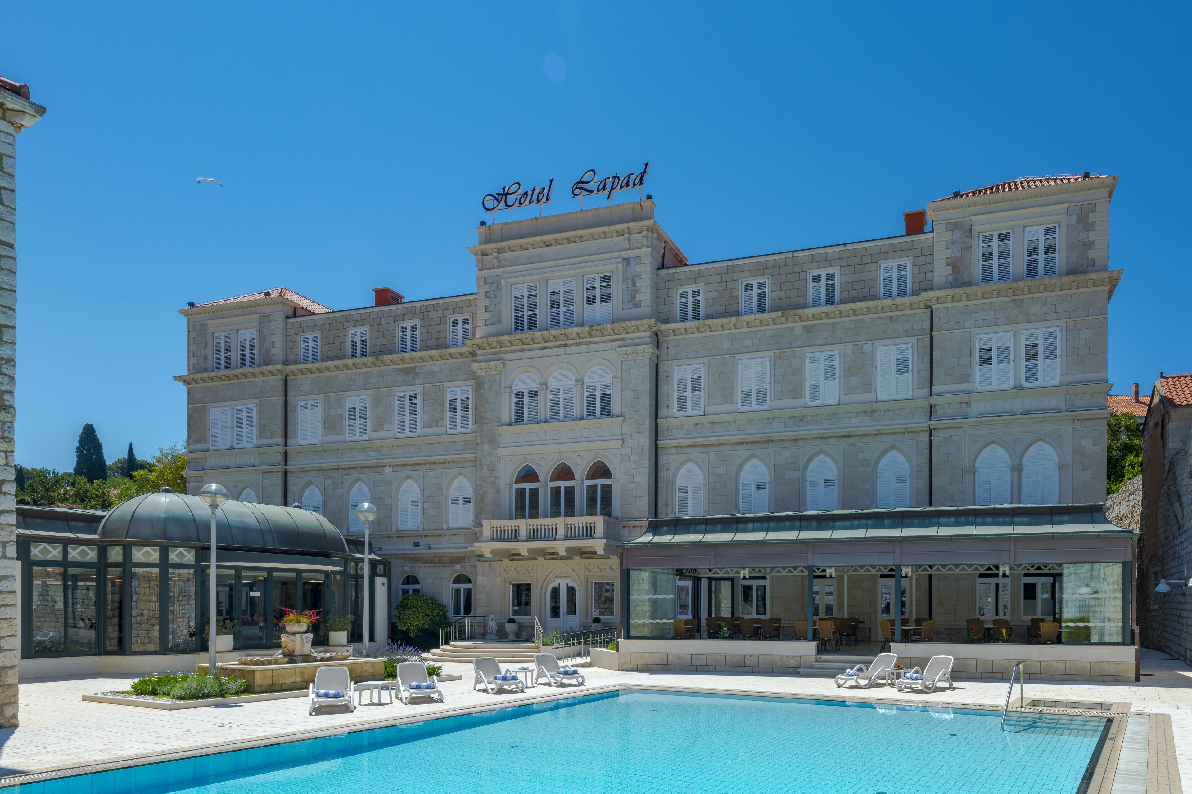 Un grande hotel con piscina, lettini da sole e una zona esterna coperta.