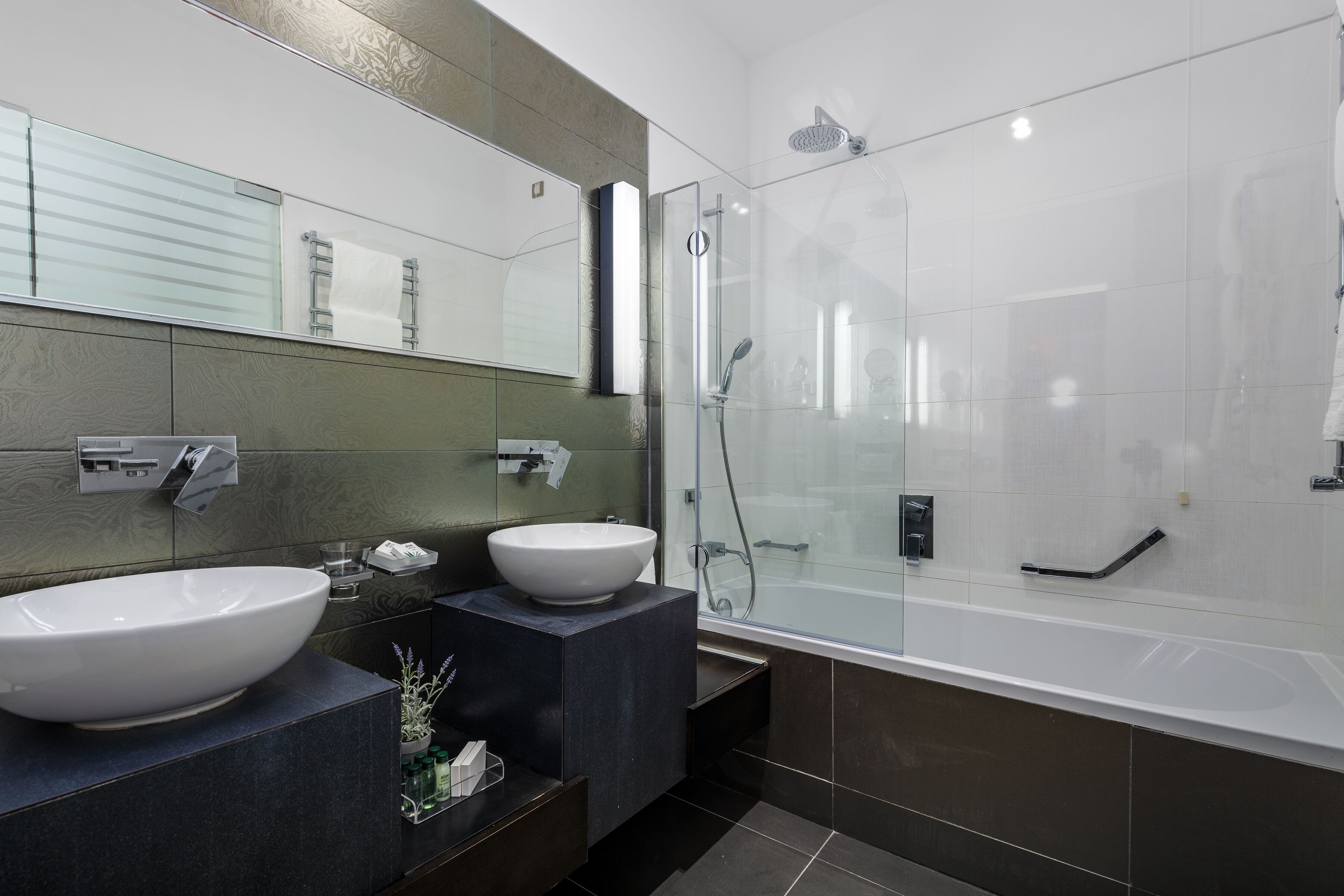 A modern bathroom with two sinks, a glass-enclosed shower, and a large mirror.
