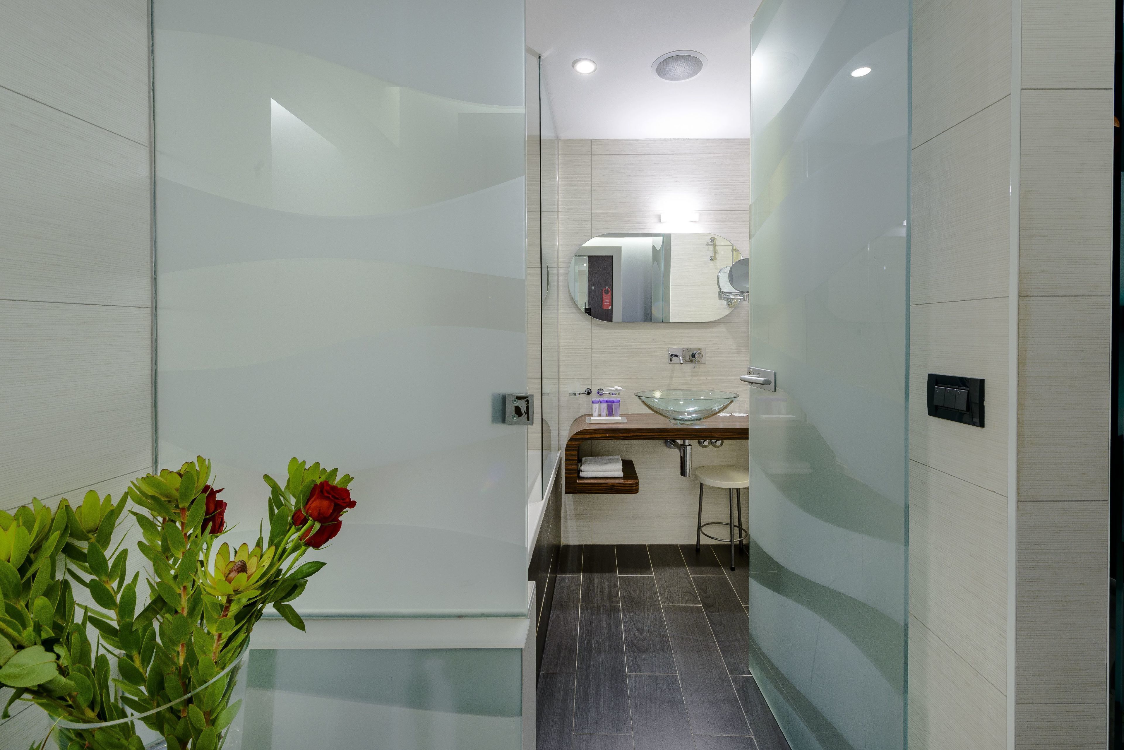 Une salle de bain moderne avec une douche à parois de verre, un lavabo en verre et un miroir au-dessus du lavabo.
