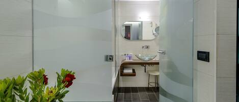 A modern bathroom with a glass shower enclosure, a glass sink, and a mirror above the sink.