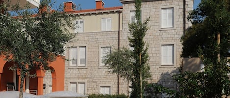 A courtyard with a stone building, a tree-lined pathway, and a small garden area.