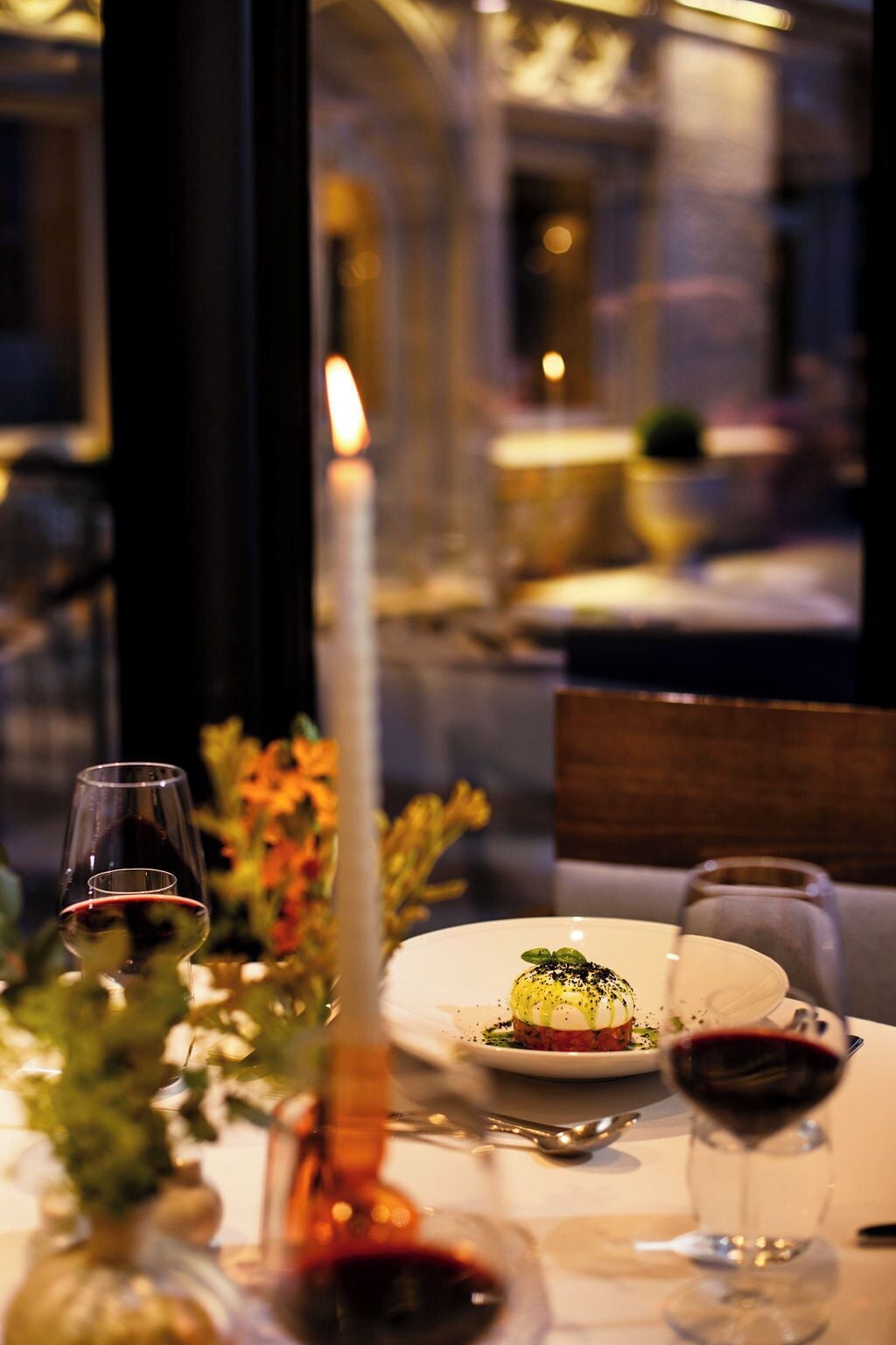Una mesa de comedor con una vela, copas de vino y un plato de comida.