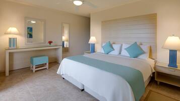 A hotel room with a large bed, a desk with a chair, a small stool, and two bedside tables with lamps.