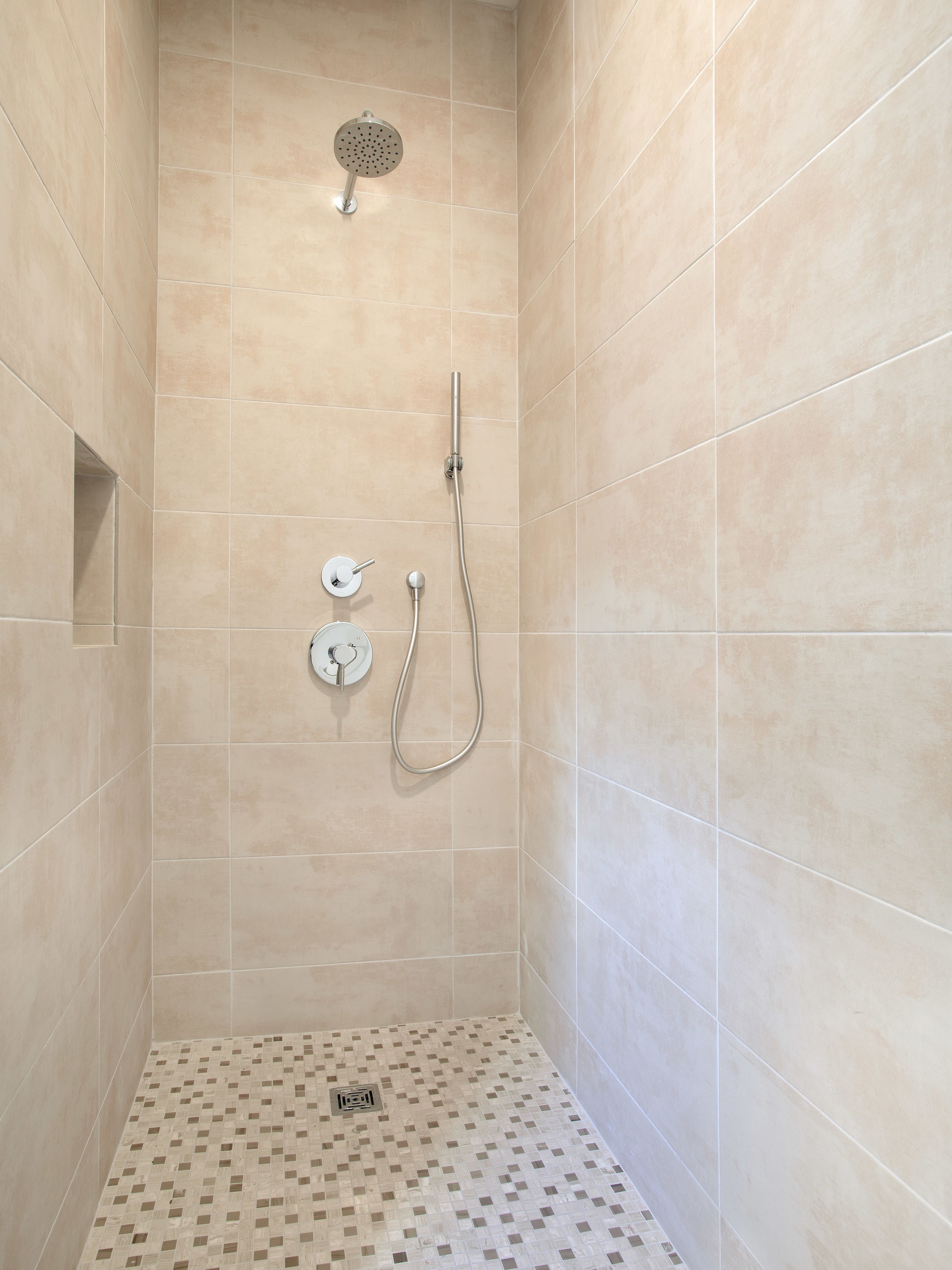A shower with a handheld showerhead and a wall-mounted faucet.