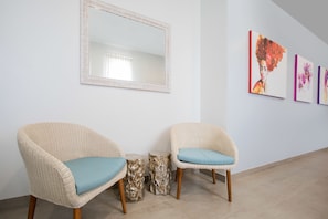 A room with two wicker chairs with blue cushions, a round wooden side table, and a large mirror on the wall.