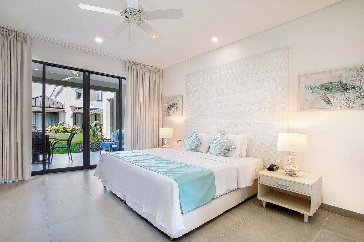 A hotel room with a bed, a nightstand, a ceiling fan, a window with curtains, and a view of the outside.