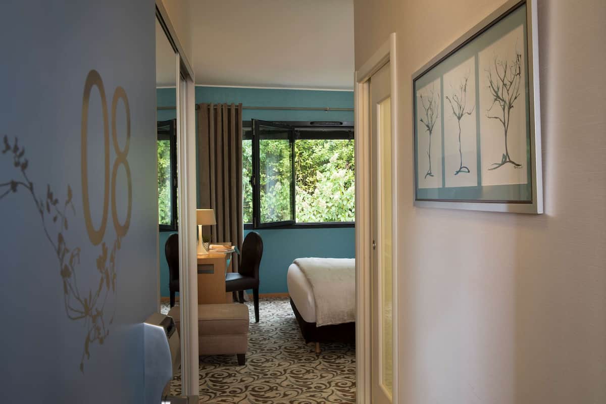 Een hotelkamer met een bed, een bureau, een stoel en een raam met uitzicht op bomen.