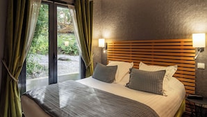 Een hotelkamer met een groot bed, een houten hoofdbord, twee bedlampen en uitzicht op groen buiten het raam.