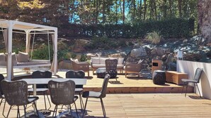 Een terras buiten met wicker meubels, een overdekte zithoek en een houten tafel.