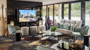 Een moderne woonkamer met een grote flatscreen televisie, comfortabele zitplaatsen en uitzicht op groen.