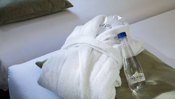 Una cama bien hecha con una toalla blanca, una botella de agua transparente y una almohada.