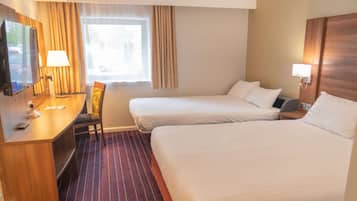 A hotel room with two beds, a desk with a chair, a TV, and a window with curtains.
